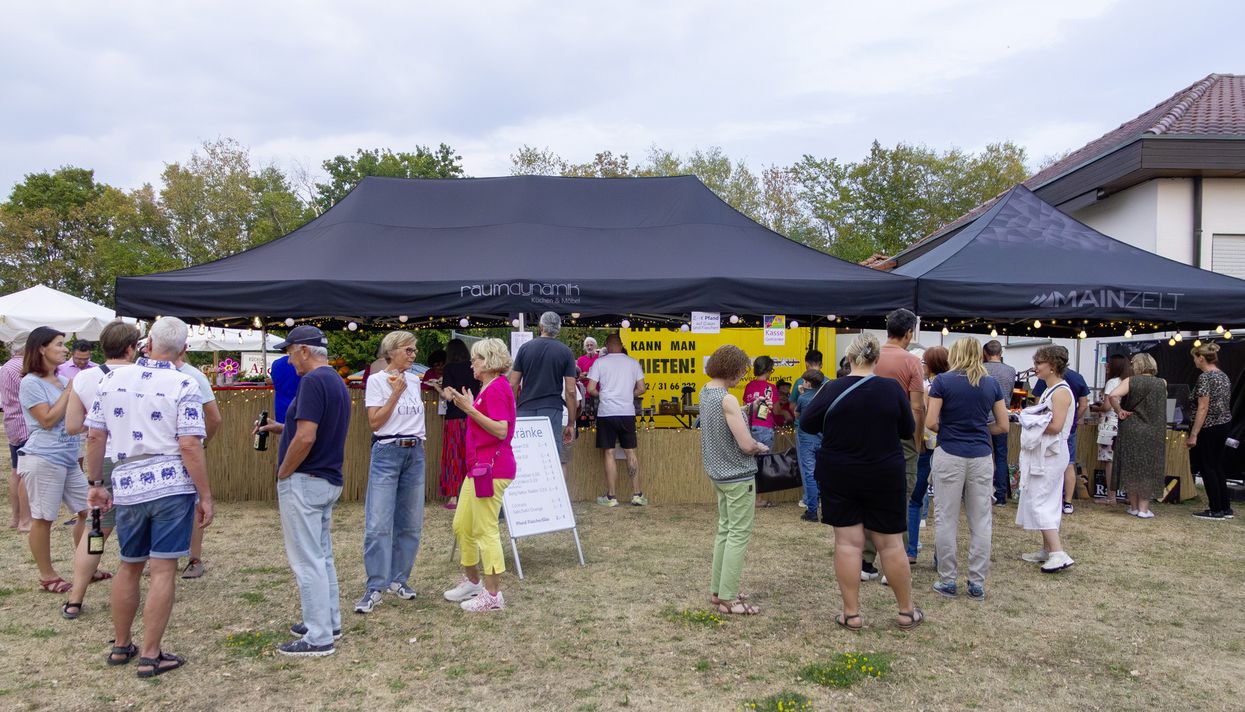 Menschen bei einer Veranstaltung im Freien auf einer Wiese. Im Hintergrund Pavillons