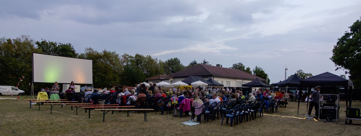 Menschen sitzen auf Stühlen vor einer Kinoleinwand beim Open-Air-Kino